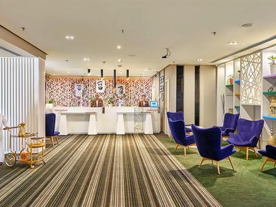 Hotel lobby met grijs tapijt, blauwe zithoek en moderne receptiebalie.