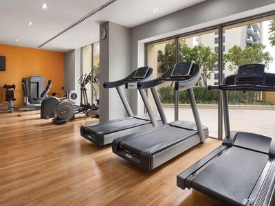 Palestra con tapis roulant e attrezzature per esercizi davanti a grandi finestre con vista all'aperto.