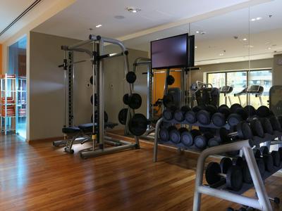 Palestra moderna dell'hotel con pesi, attrezzi per allenamento e pavimento in legno.