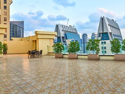 Groot terras met tafels, stoelen en bloempotten voor moderne stadsgebouwen onder een bewolkte hemel.