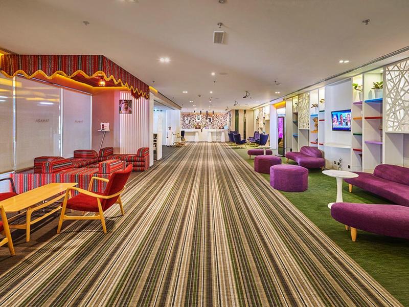 Moderne hotelgang met gestreept tapijt en comfortabele rode en paarse zitplaatsen.