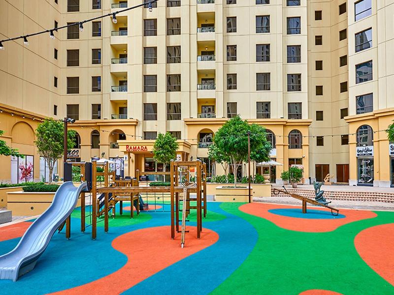 Kleurrijke speeltuin met glijbaan en klimrek in een hotelbinnenplaats.