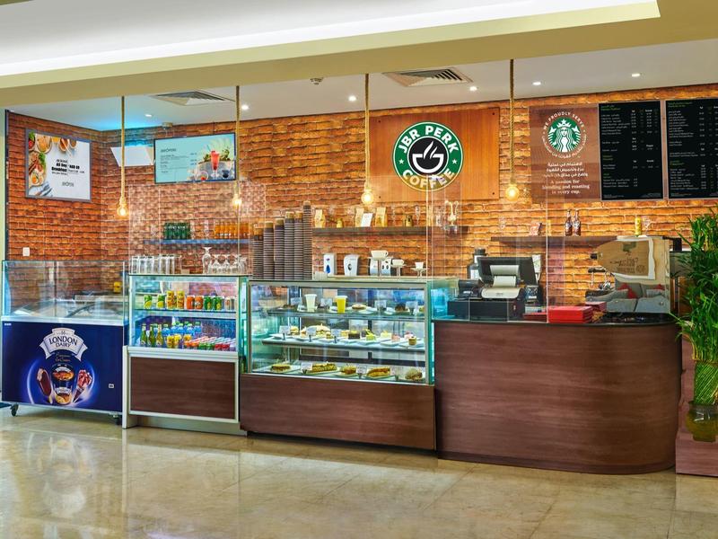 Modern café met toonbank, gebakjes en dranken in een lichte binnenruimte.