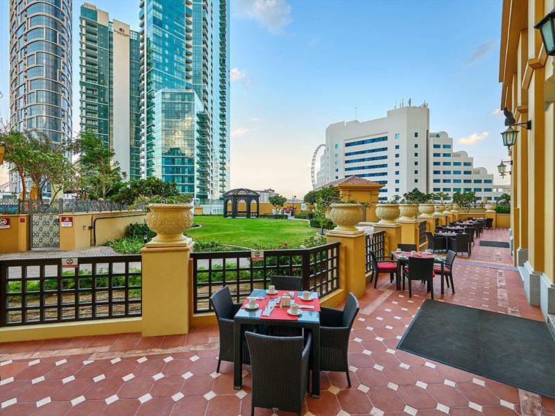 Buitenterras van een hotel met tafels, stoelen en uitzicht op wolkenkrabbers bij zonnig weer.