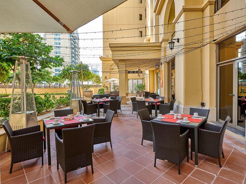 Buitengebied van een café met tafels en stoelen op een terras naast een gebouw.