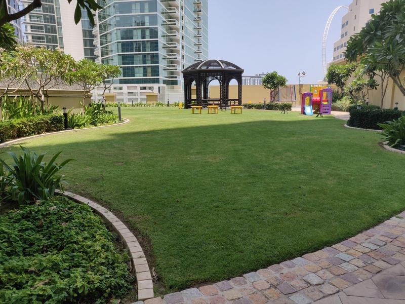 Groen grasveld met een prieel en zitplaatsen in een wooncomplex.