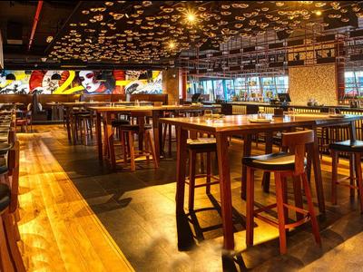 Modern restaurant area with wooden tables, bar stools, and decorative ceiling lighting.