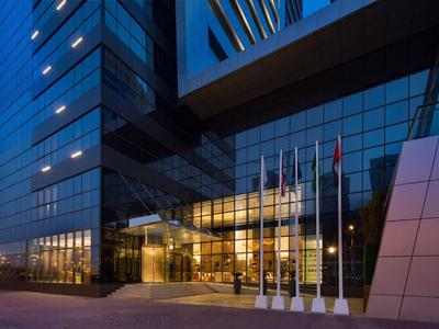 Entrance of a modern hotel at dusk with glass facade and illuminated interiors.