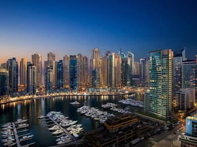 View of an illuminated marina with skyscrapers and yachts at night.