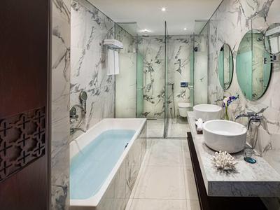 Modern bathroom with marble walls, bathtub, two sinks, and large glass shower.