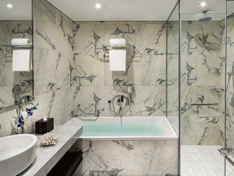 Modern bathroom with marble tiles, bathtub, sink, and shower enclosure.