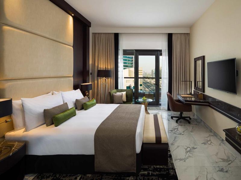 Modern hotel room with double bed, TV, and balcony seating area.