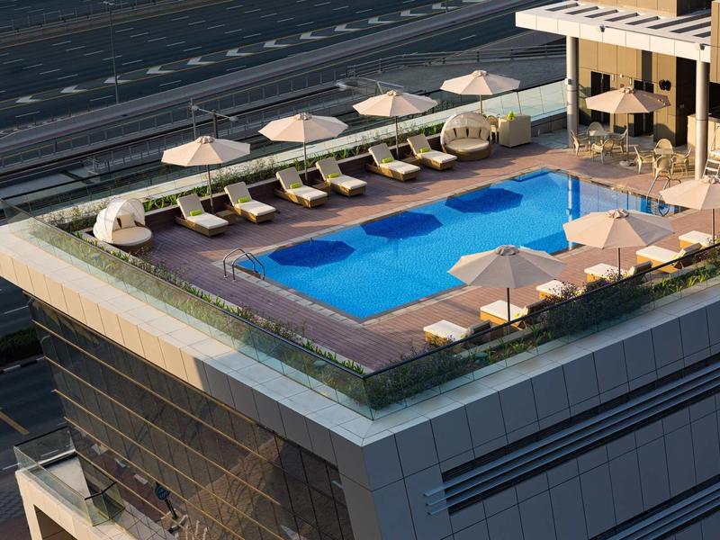 Rooftop pool with lounge chairs and umbrellas on a modern high-rise building.