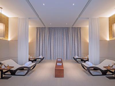 Symmetrisch angeordnete Liegen mit Kissen in einem ruhigen, minimalistisch gestalteten Raum mit Vorhängen.