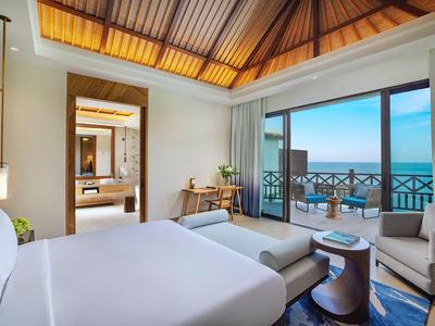 Helles Hotelzimmer mit großem Bett, Stühlen und Balkon mit Meerblick.