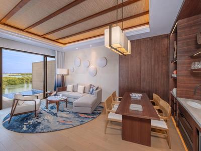 Moderner Wohnbereich mit hellen Möbeln, großem Fenster und angrenzendem Essbereich in warmen Tönen.