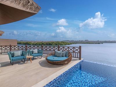 Terrasse mit Pool, Sitzbereich und Blick auf einen See unter blauem Himmel.