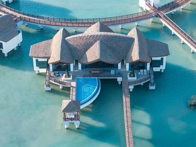 Luxuriöse Überwasserbungalows mit Pool auf türkisfarbenem Wasser und Holzstegen im Resort.