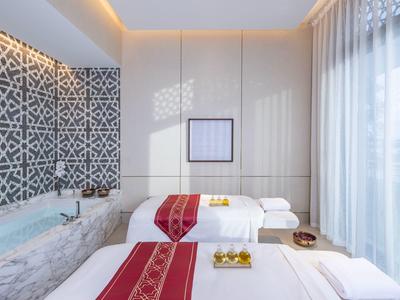 Helles Spa-Zimmer mit zwei Massageliegen, dekorativen Teppichen und großen Fenstern mit Gardinen.