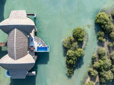 Luftaufnahme eines Hauses auf Stelzen über klarem Wasser neben grüner Vegetation.