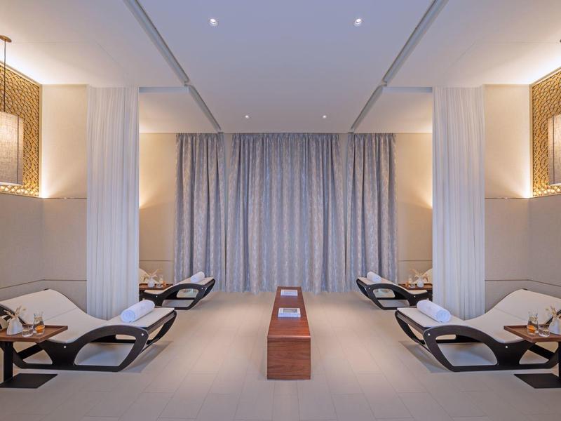 Symmetrisch angeordnete Liegen mit Kissen in einem ruhigen, minimalistisch gestalteten Raum mit Vorhängen.