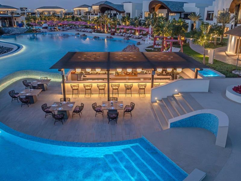 Abendaufnahme eines beleuchteten Pools mit Bar und Sitzgelegenheiten in einem Hotelresort.