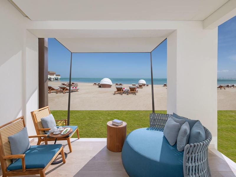 Offener Lounge-Bereich mit Sitzmöbeln und Blick auf Strand und Meer bei klarem Himmel.