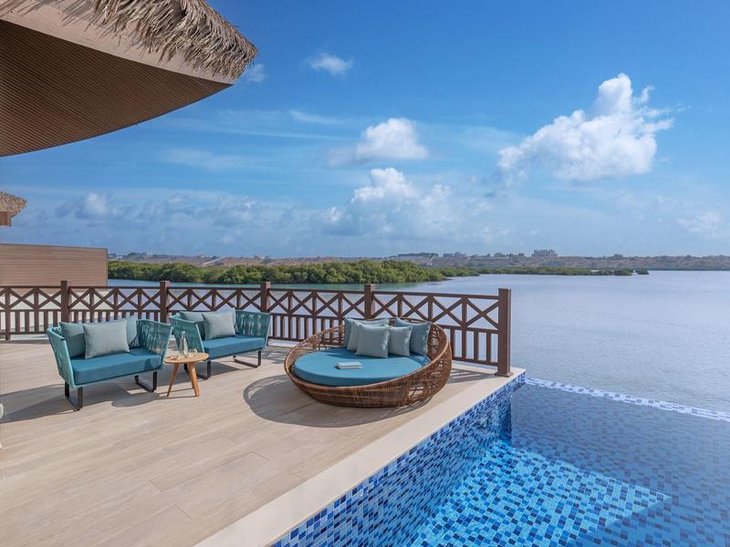 Terrasse mit Pool, Sitzbereich und Blick auf einen See unter blauem Himmel.