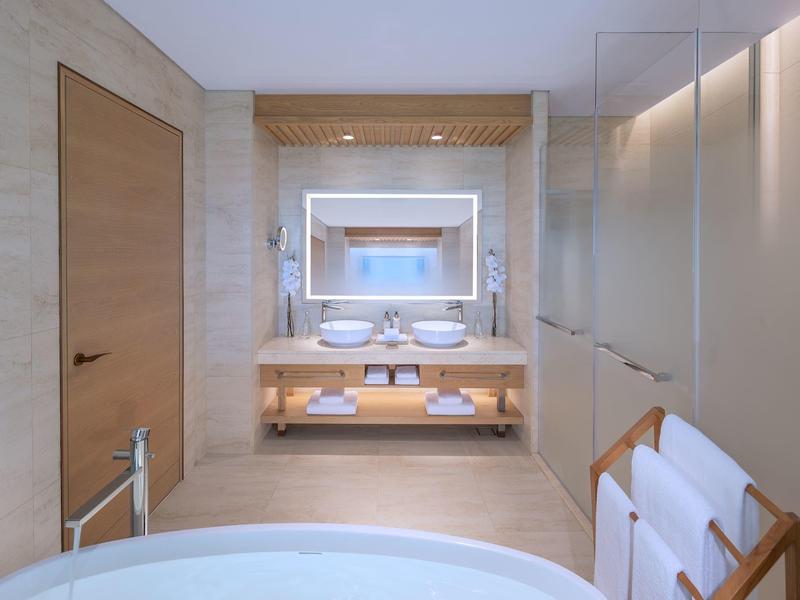 Modernes Badezimmer mit Doppelwaschbecken, beleuchtetem Spiegel und freistehender Badewanne.