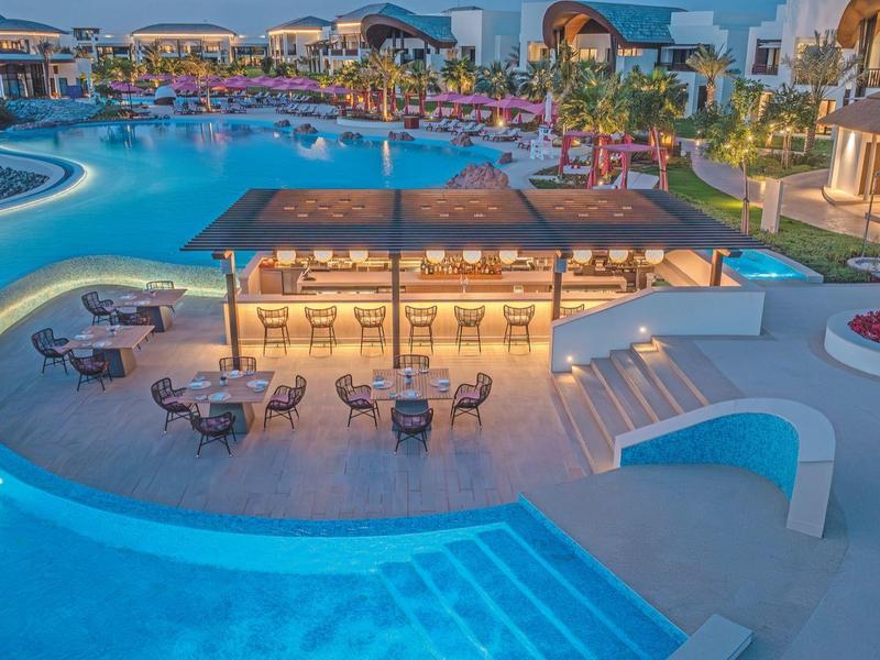 Moderner Hotelpool mit Bar und Sitzgelegenheiten bei Sonnenuntergang.