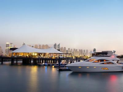 Luxusyacht liegt im Hafen neben einer modernen Marina mit Gebäuden im Hintergrund bei Sonnenuntergang.