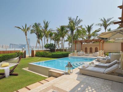 Luxurious pool area with loungers, palm trees, and sea view under clear sky