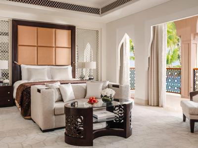 Elegantes Hotelzimmer mit großem Bett, bequemen Sesseln und Zugang zu einem Balkon mit Blick auf Palmen.