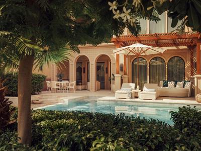 Luxurious patio with pool, seating areas, and lush garden surroundings in warm light.