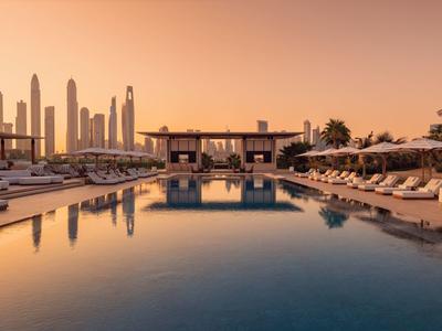 Luxuriöser Poolbereich eines Hotels mit Sonnenliegen und Skyline im Sonnenuntergang.