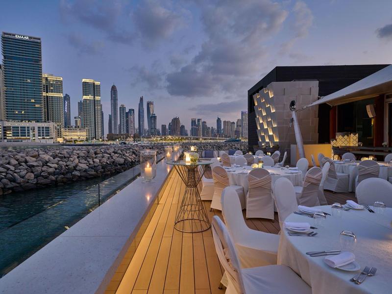 Outdoor-Restaurant mit gedeckten Tischen und Blick auf die Skyline bei Abenddämmerung