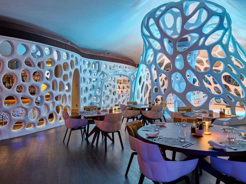 Modern eingerichteter Hotelrestaurantbereich mit organisch geformten, beleuchteten Wänden und gemütlichen Sitzplätzen.