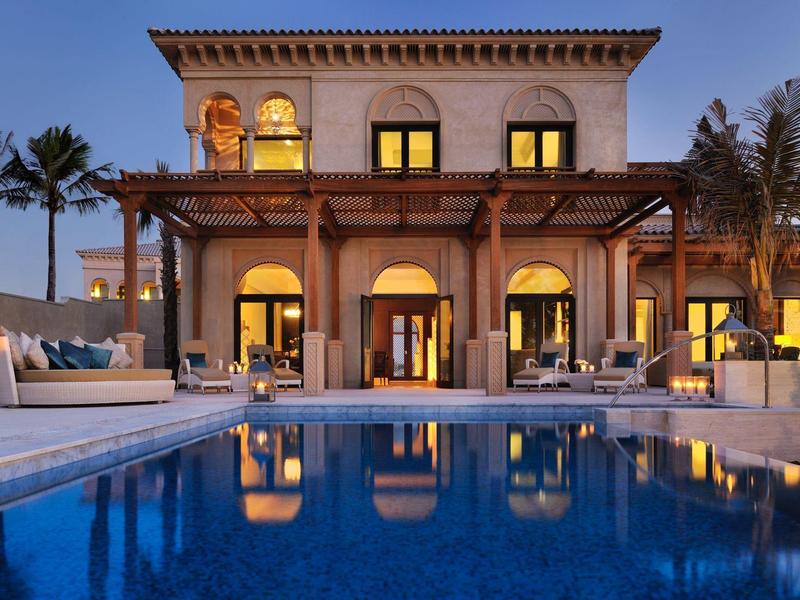 Luxuriöse Villa mit beleuchtetem Pool und Palmen im Abendlicht