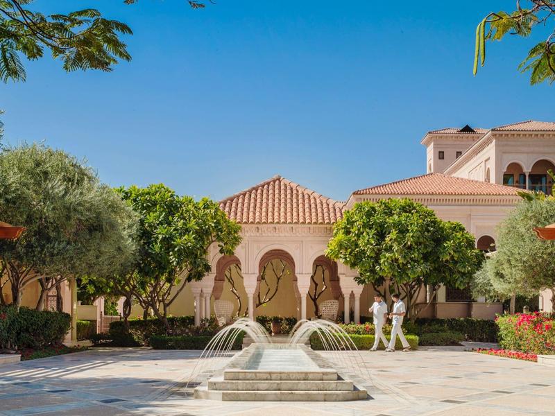 Innenhof eines Hotels mit Springbrunnen, umgeben von Bäumen und mediterraner Architektur.