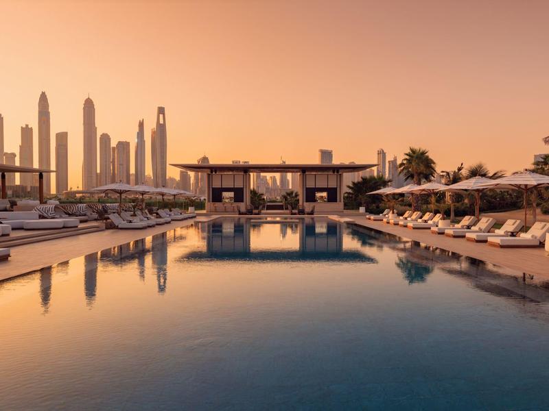 Luxuriöser Poolbereich eines Hotels mit Sonnenliegen und Skyline im Sonnenuntergang.