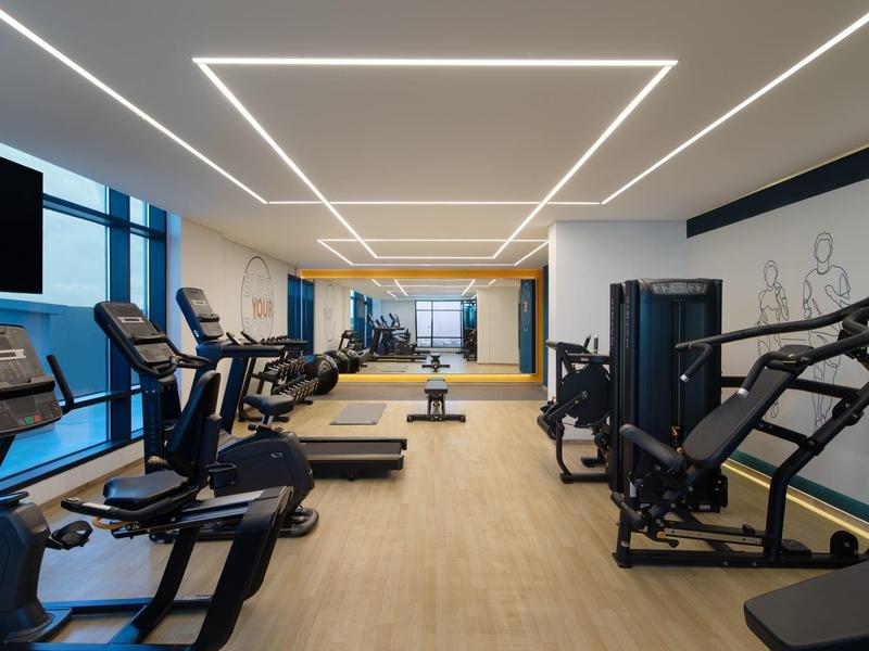 Moderner Fitnessraum mit Cardiogeräten, Kraftmaschinen und großen Fenstern für Tageslicht.