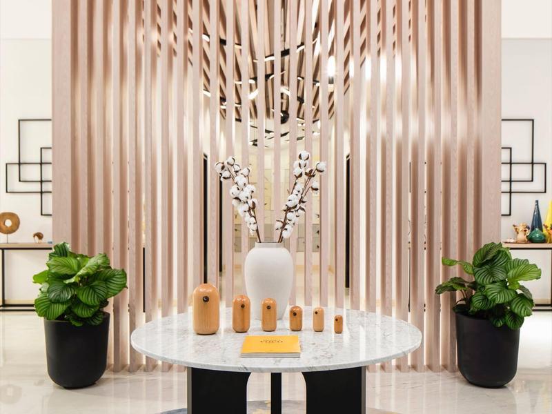 Moderner Raum mit rundem weißen Tisch, dekorativen Vasen, Pflanzen und Holzlattenwand im Hintergrund.