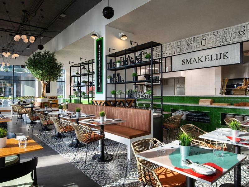 Modernes Café mit grünen Akzenten, braunen Sitzbänken und hölzernen Tischen, viel Tageslicht.