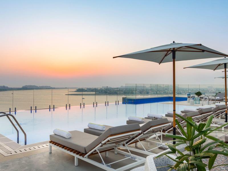 Schwimmbad mit Liegestühlen und Sonnenschirmen am See bei Sonnenuntergang.