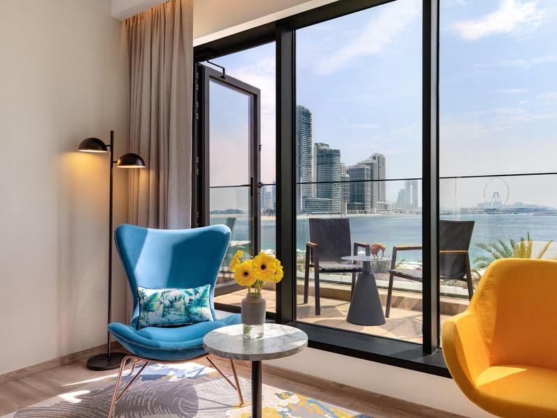 Helles Wohnzimmer mit blauen und gelben Sesseln, Slide-Glasfenster und Stadtblick am Fluss.