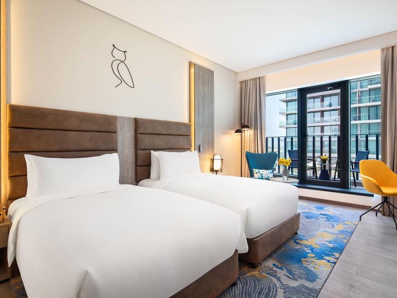 Helles Hotelzimmer mit zwei Betten, modernen Möbeln und großem Fenster mit Blick auf Außenbereich.