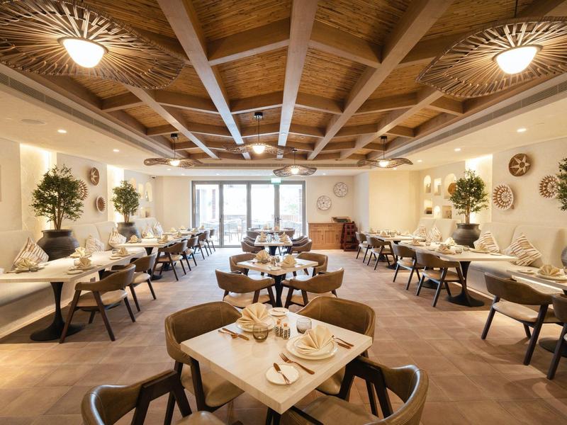 Helles Hotelrestaurant mit Holzbalkendecke, runden Tischen und moderner Einrichtung.