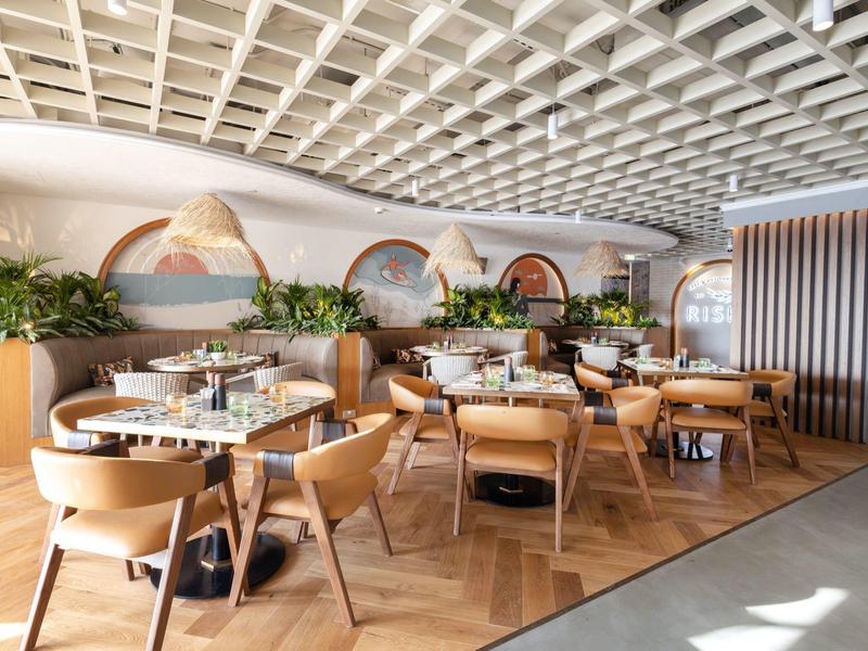 Moderner und heller Hotelrestaurantbereich mit Holzstühlen und Tischen, gezielt grünen Pflanzen und Wandkunst.