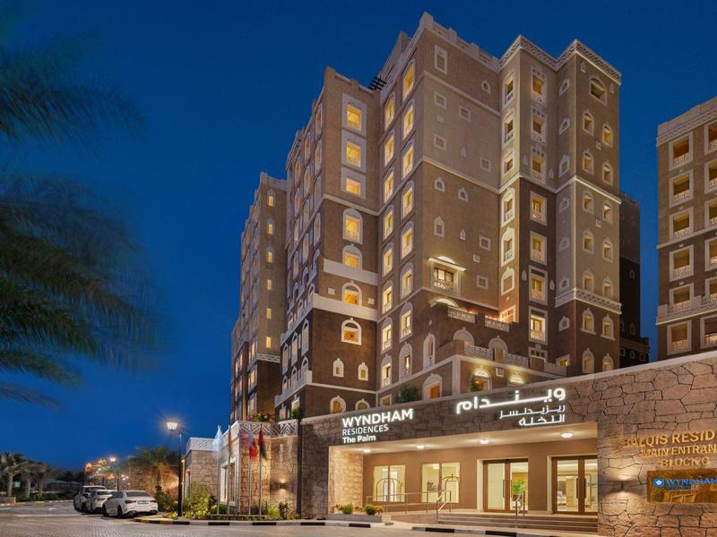 Beleuchtetes Wyndham Hotel bei Nacht mit mehrstöckigem Gebäude und gepflastertem Vorderbereich.