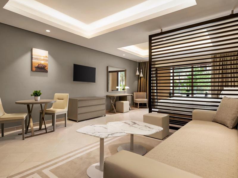 Modern eingerichtetes Hotelzimmer mit Sitzbereich, TV und Schreibtisch in warmen Farben.